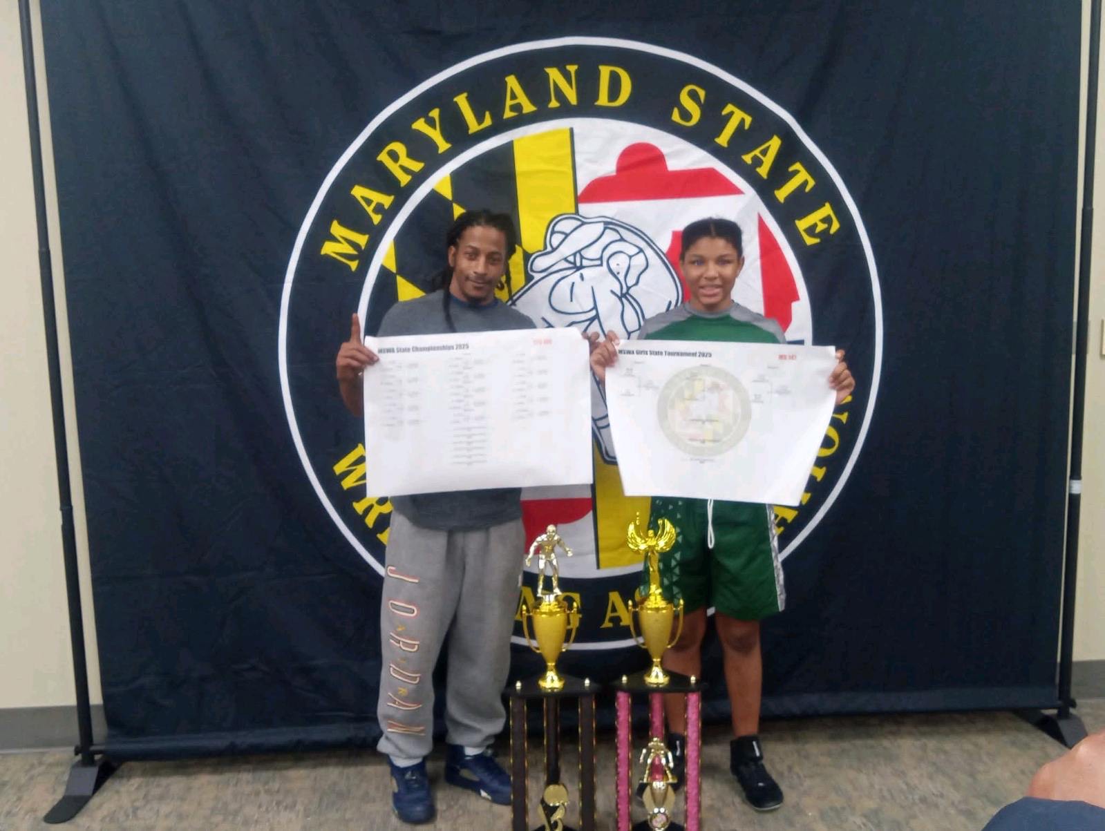 Coach Coles and a CWA state champion holding tournament brackets and trophies