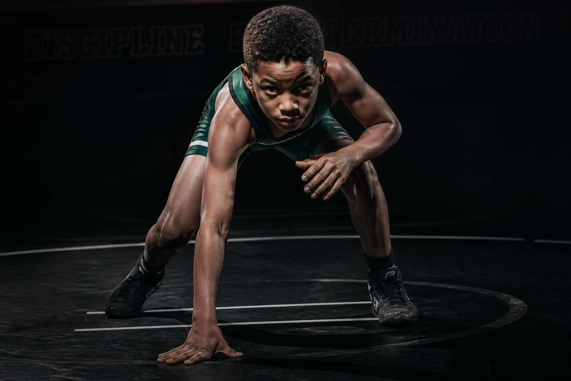 Young wrestler in a forest green singlet in a training stance
